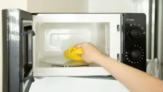 Ręka z żółtą ściereczką czyści wnętrze otwartej mikrofalówki. Prosty sposób, jak wyczyścić mikrofalówkę.