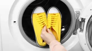 Ręka wkłada żółte trampki do bębna pralki. Czy można suszyć buty w suszarce?